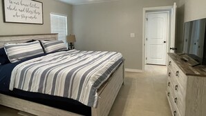 A bedroom with a bed, a ceiling fan, a dresser, and a wall-mounted TV.