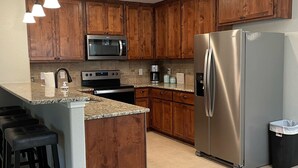 A kitchen with wooden cabinets, a stainless steel refrigerator, a microwave, a stove, and a coffee maker.