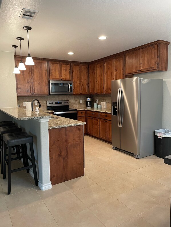 A kitchen with wooden cabinets, a stainless steel refrigerator, a microwave, a stove, and a coffee maker.