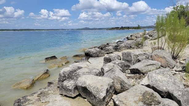 A rocky shoreline with clear water and a distant view of land.