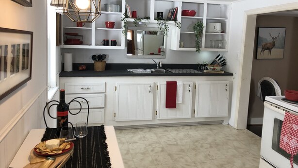 Una cocina con armarios blancos, encimera negra y una lámpara colgante. Hay un tazón rojo en la repisa y una foto enmarcada en la pared.