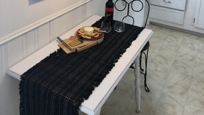 Una cocina con armarios blancos, una mesa de comedor con camino de mesa negro, cuadros en la pared y una lámpara colgante.
