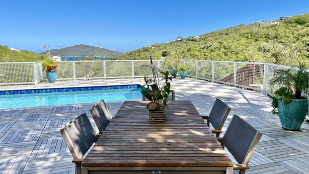 Eine Holzterrasse mit einem Pool, umgeben von weißen Zäunen und Kübelpflanzen.