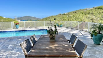 Une terrasse en bois avec une piscine, entourée de clôtures blanches et de plantes en pot.
