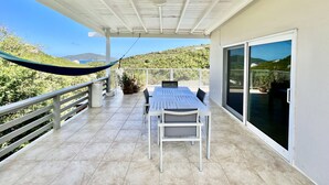 Eine überdachte Terrasse mit Tisch und Stühlen, einer Hängematte und Blick auf eine hügelige Landschaft.