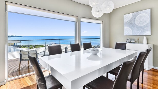 A modern dining area with a large white table, black chairs, and a view of the ocean. - Robe Highview (Robe)