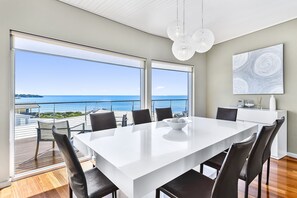 A modern dining area with a large white table, black chairs, and a view of the ocean. - Robe Highview (Robe)