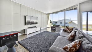 A modern living room with a large flat-screen TV, a grey sofa with patterned cushions, a black coffee table, and a black accent chair. - Robe Highview (Robe)