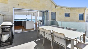A modern outdoor dining area with a large table and chairs, a grill, and a view of the sea. - Robe Highview (Robe)