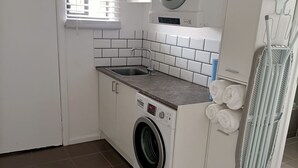 Une petite buanderie équipée d’un lave-linge, d’un évier et d’un étendoir.