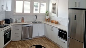 Une cuisine moderne avec des meubles blancs, des appareils en acier inoxydable, un plan de travail en marbre et un coin repas agrémenté d’une chaise noire.