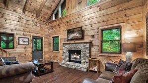 L’intérieur d’une cabane en rondins, avec une cheminée en pierre, des murs en bois et un coin salon confortable.