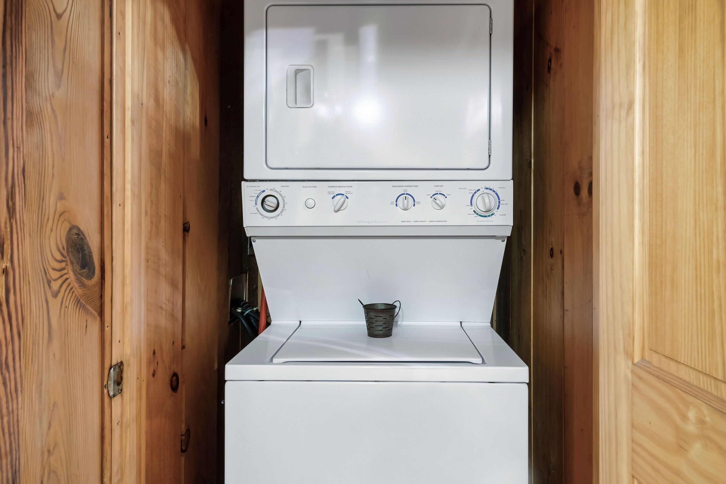 Une petite machine à laver blanche, intégrée dans un meuble en bois, avec un petit récipient en métal placé sur le dessus.