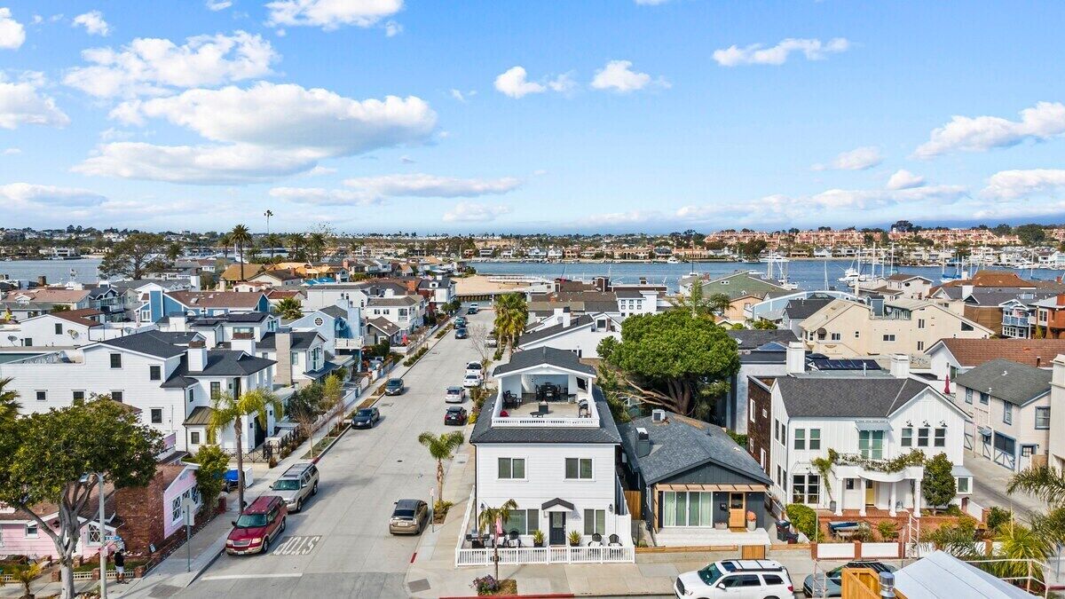 A residential street with houses, parked cars, and a marina in the background.