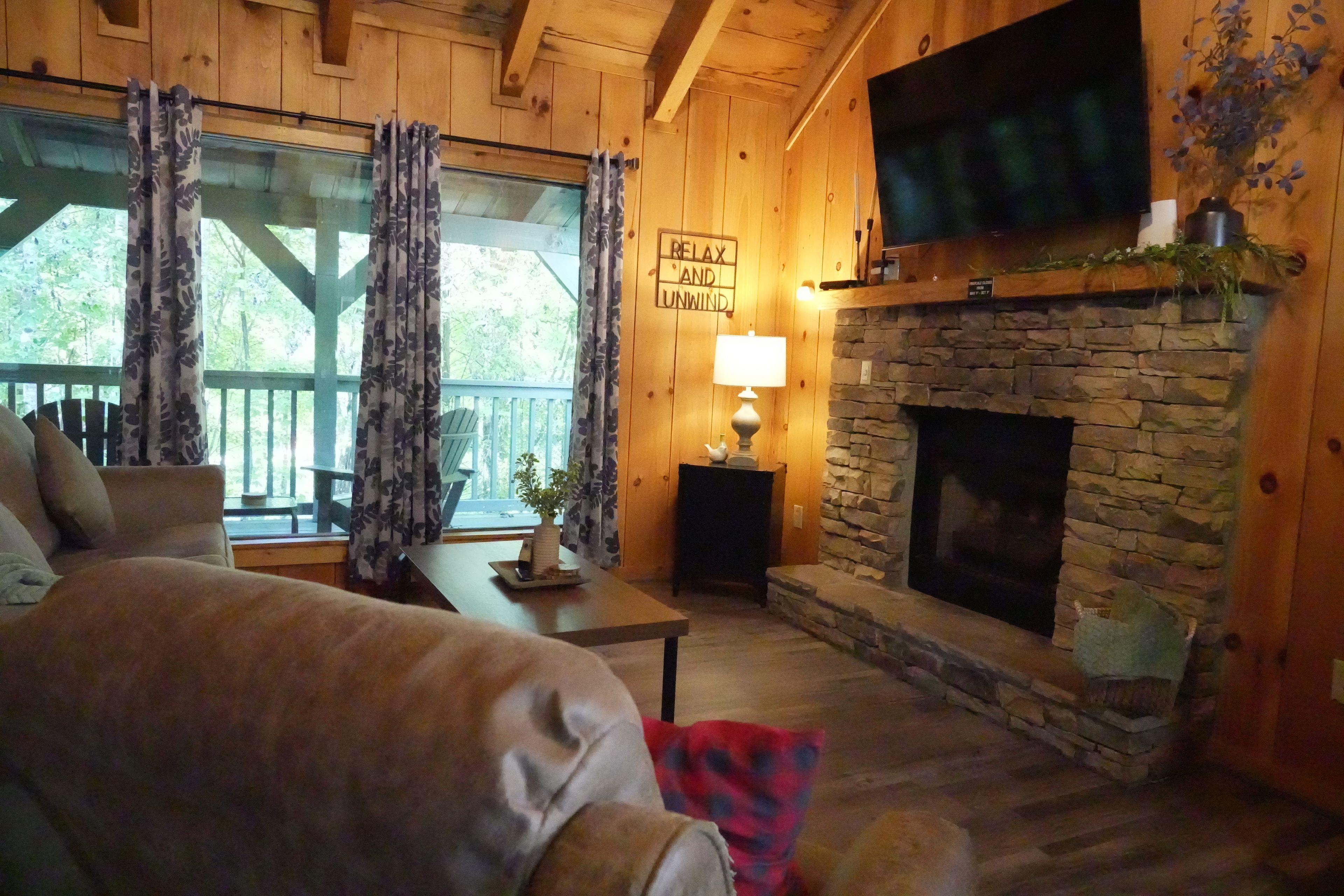Un salon chaleureux avec une cheminée en pierre, des murs en bois, un canapé et un téléviseur fixé au-dessus de la cheminée.