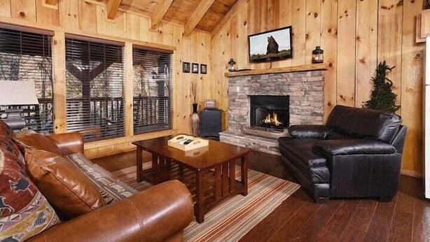 A cozy living room with a stone fireplace, leather sofas, and a large window with blinds. - Moonshine Holler (Sevierville)