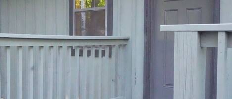 Una cabaña de madera con un porche, una puerta y dos ventanas.
