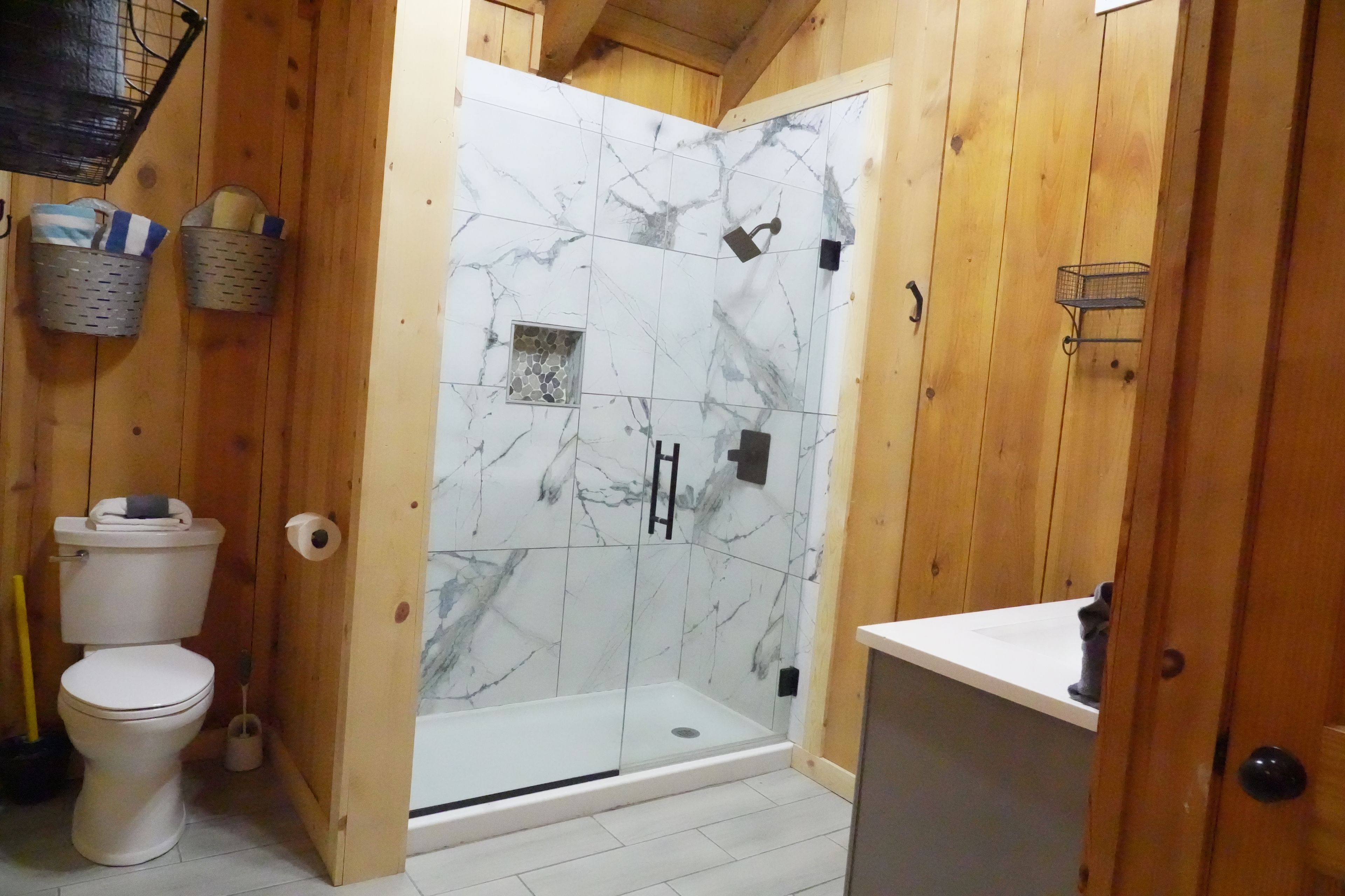 A wooden interior with a glass-enclosed shower, a toilet, and a sink.
