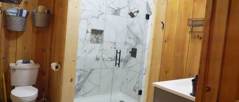 A wooden interior with a glass-enclosed shower, a toilet, and a sink.