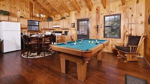 A wooden interior with a pool table, dining area, and kitchen. - Moonshine Holler (Sevierville)