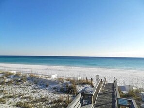 Ein Strand mit einer Holzpromenade, die zum Wasser führt, feinem Sand und blauem Himmel.