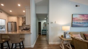 A modern kitchen with a stainless steel refrigerator, wooden flooring, and a dining area with two chairs. - Charming Beach Cottage, Beach Chair Service Included. Snowbirds special rates! (Miramar Beach)
