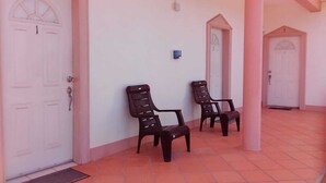 Un espace extérieur abrité comprenant deux chaises, une porte blanche et un sol carrelé.