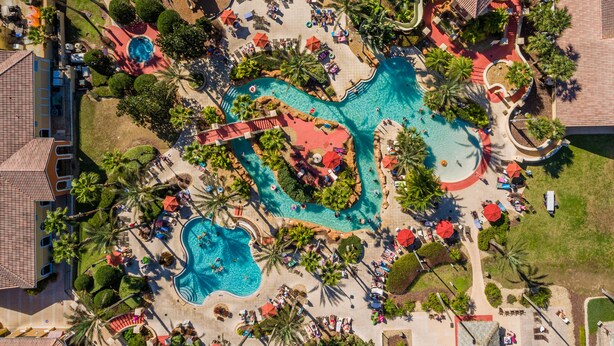 Vista aérea de un resort con varias piscinas, palmeras y tumbonas.