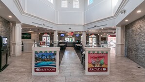 Un amplio atrio con zona de piscina, área de juegos arcade y señalización de baños.