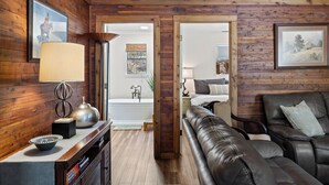 A room with wooden walls, a leather sofa, a small table with a lamp, and a framed picture on the wall. - Private & Seculded Cabin on Comanche Creek with 73 Acres to Roam (Llano)
