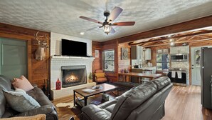 A cozy living room with a fireplace, leather sofas, and a television mounted above it. - Private & Seculded Cabin on Comanche Creek with 73 Acres to Roam (Llano)