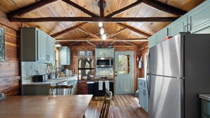 A cabin-style kitchen with wooden beams, a dining table, and built-in appliances. - Private & Seculded Cabin on Comanche Creek with 73 Acres to Roam (Llano)