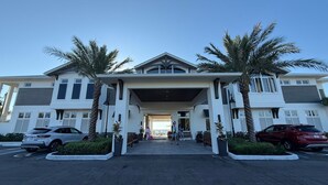 L’entrée d’un hôtel moderne, avec une allée couverte, des palmiers et des voitures garées.