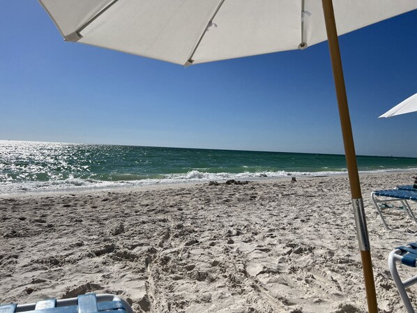 A beach with a sandy shore, a clear blue sky, and a white umbrella.