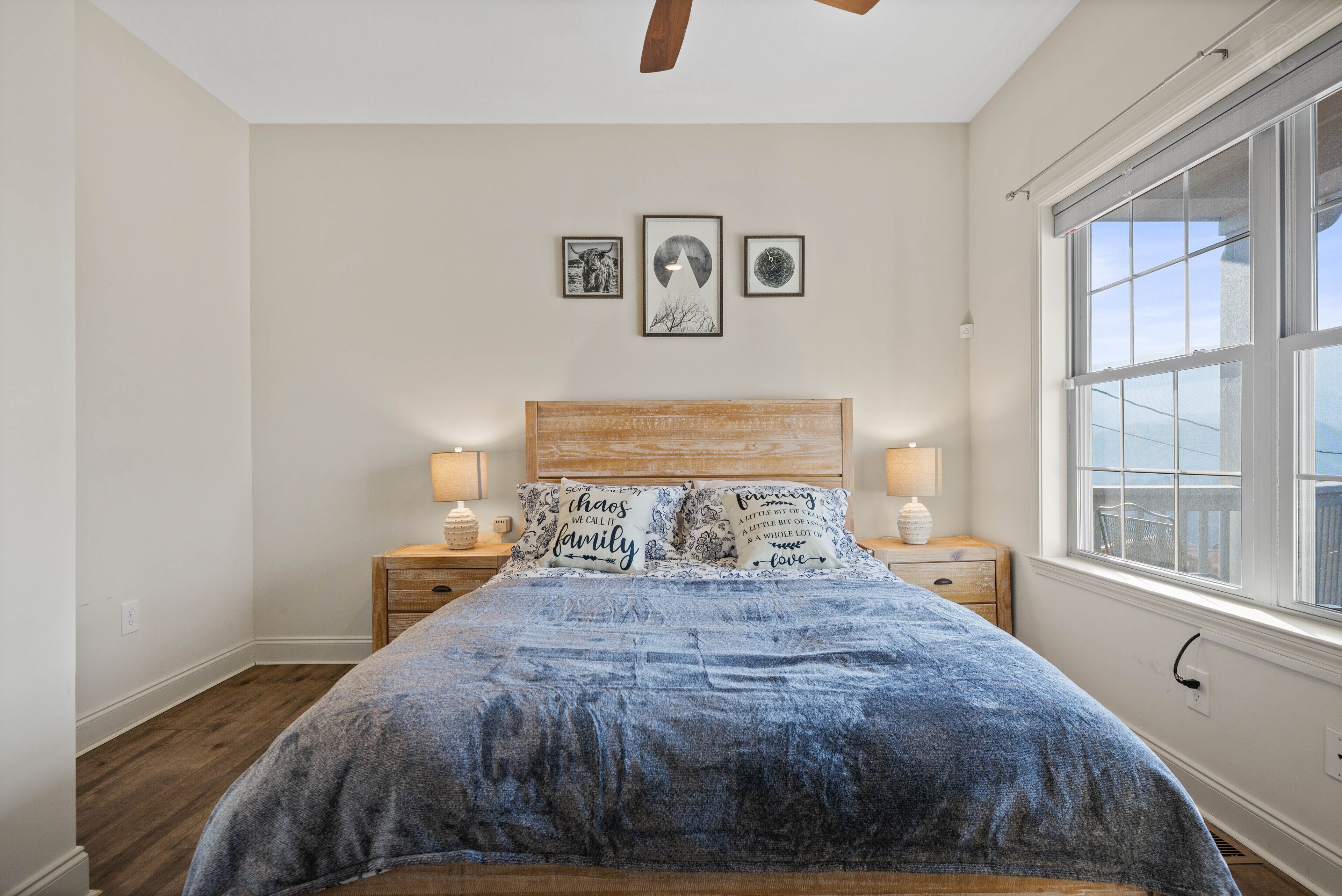 A bedroom with a wooden headboard, a large bed with a blue blanket, two bedside tables with lamps, and three framed pictures on the wall.