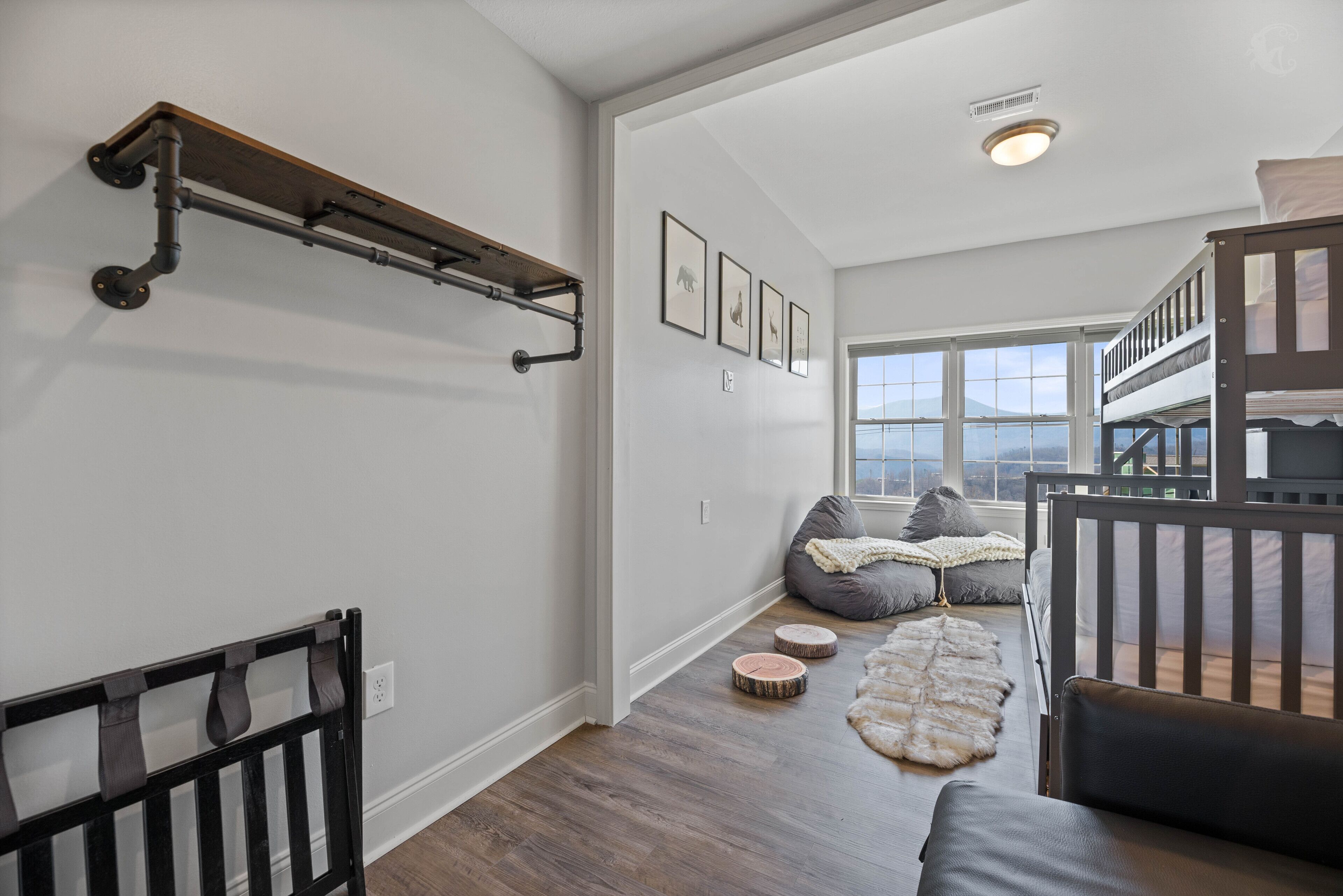 A spacious room with a high ceiling, a wooden floor, a bunk bed, a seating area with cushions, and a large window offering a view.
