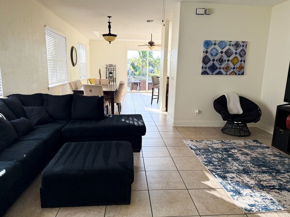 A living room with a sectional sofa, a coffee table, a patterned rug, a dining area with a table and chairs, and a ceiling fan.