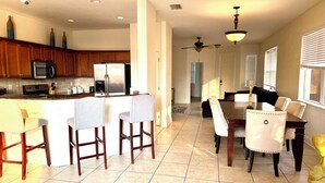 A spacious kitchen with a central island, bar stools, a dining table with chairs, and a ceiling fan. - Cozy home on the water with plenty of sleep space (Fort Myers)