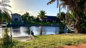 A riverside view with a house, palm trees, and a grassy area. - Cozy home on the water with plenty of sleep space (Fort Myers)