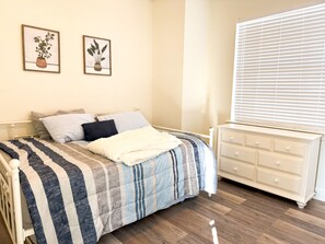 A bedroom with a bed, a dresser, and two framed plant pictures on the wall.