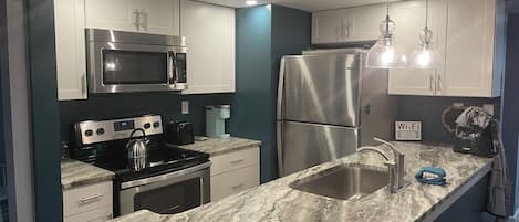 A modern kitchen with stainless steel appliances, a marble countertop, and a built-in sink.