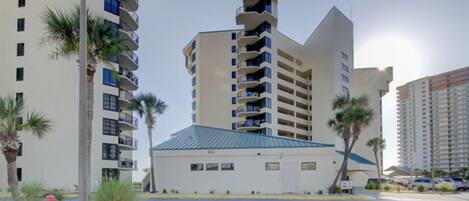 A modern multi-story building with balconies, a parking lot, and palm trees.