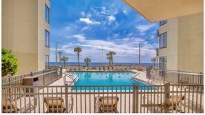 A pool area with a view of the ocean, surrounded by a fence, and a building on one side. - Penthouse Condo with spectacular views and sunsets (Panama City Beach)