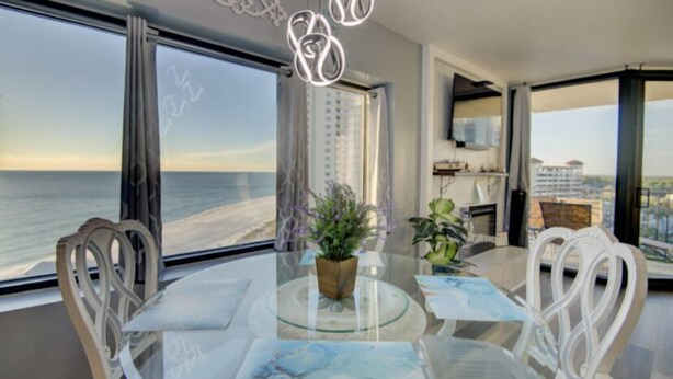 A modern dining area with a glass table, white chairs, and a view of the ocean. - Penthouse Condo with spectacular views and sunsets (Panama City Beach)