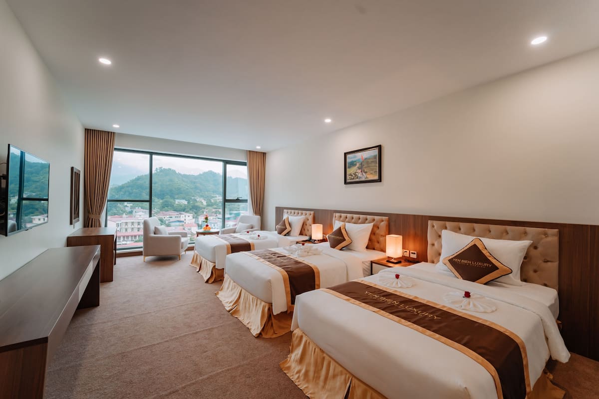 Een hotelkamer met drie bedden, een bureau, een stoel en een groot raam met uitzicht op bergen.