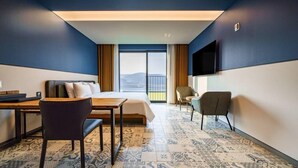 Quarto de hotel com cama, escrivaninha, cadeira, televisão e vista para o exterior.