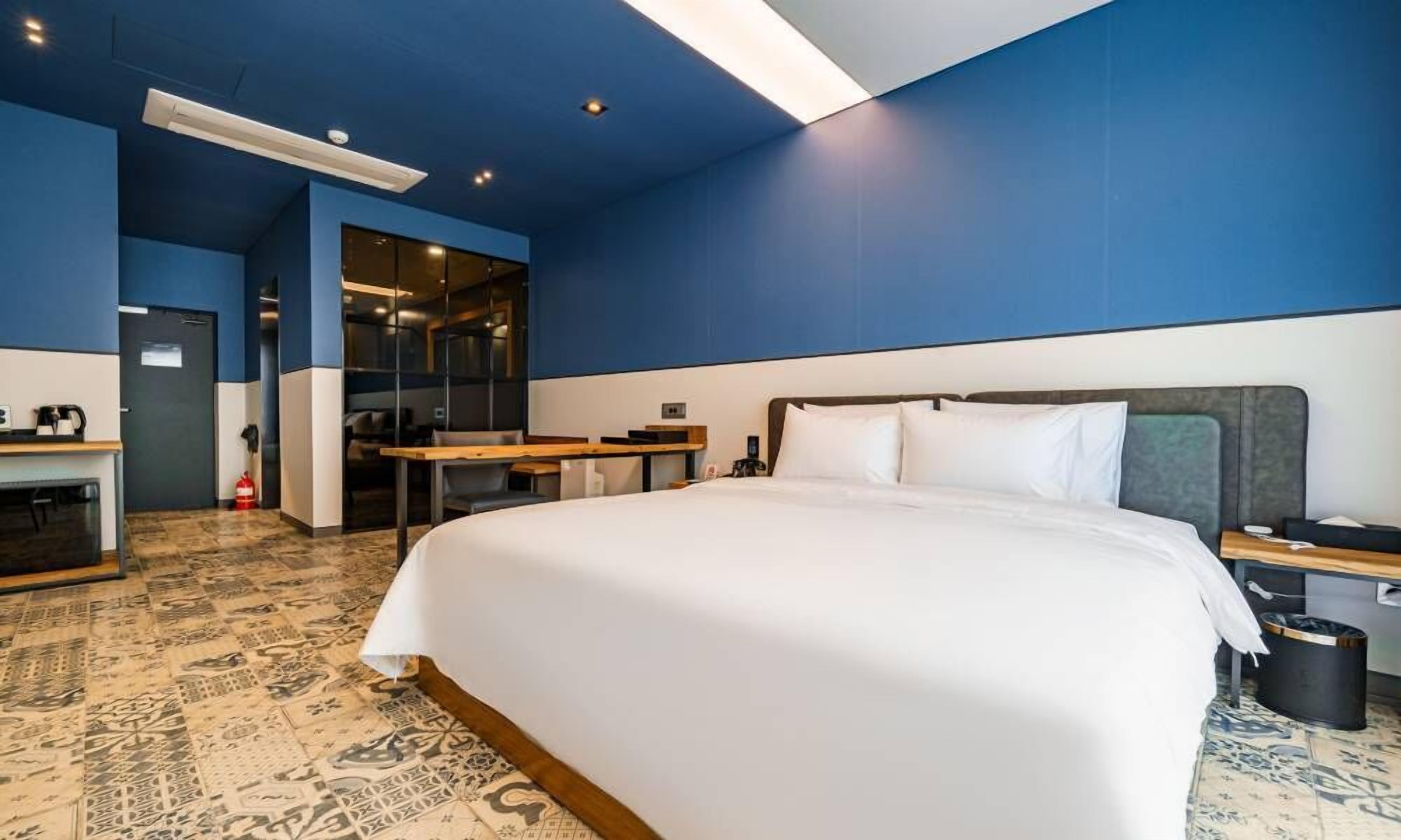 A hotel room with a large bed, a desk, a chair, and a small table.
