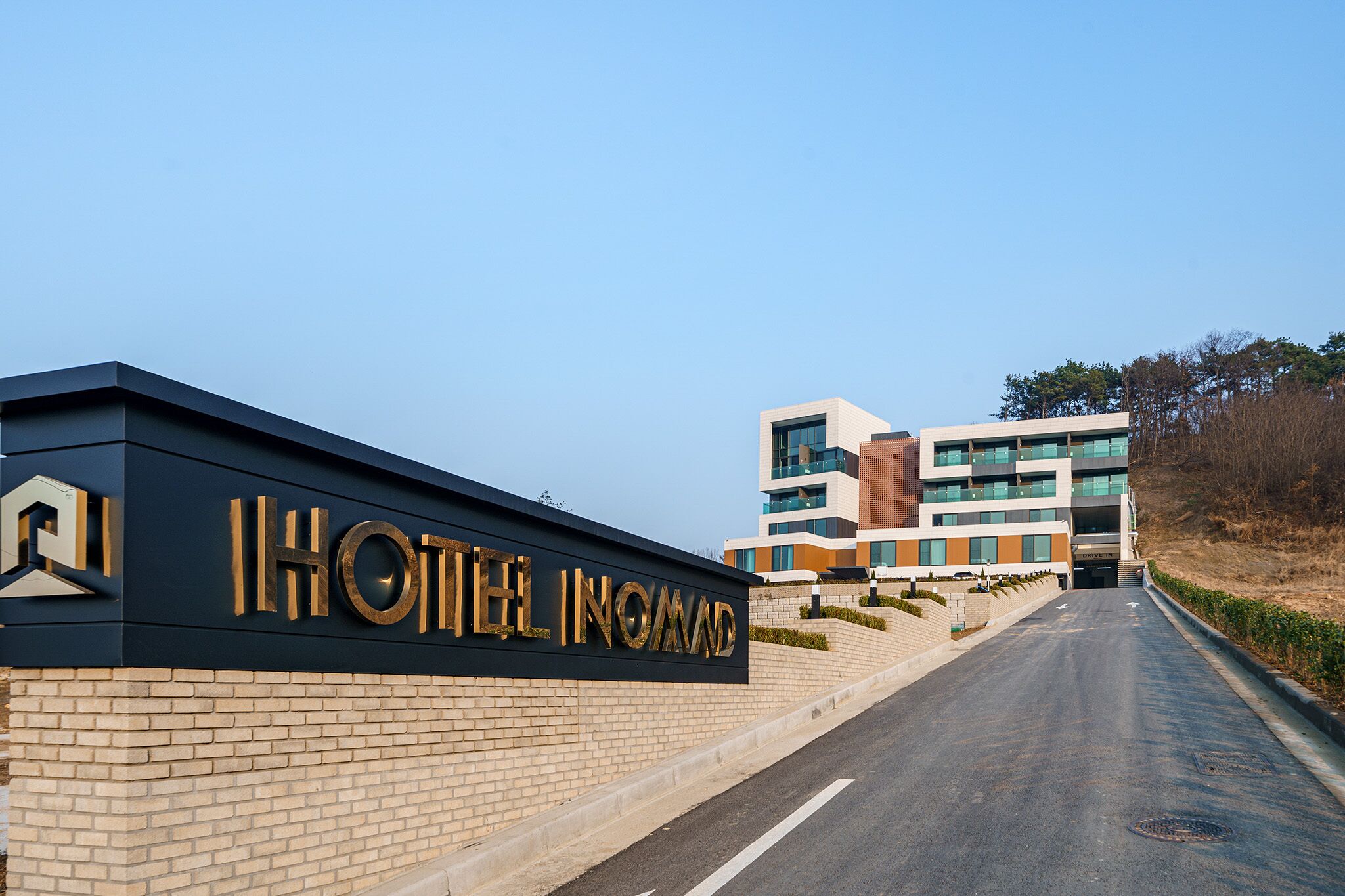 A hotel entrance with a prominent sign, a modern building in the background, and a clear sky.
