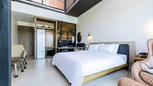 Quarto de hotel moderno com uma cama grande, uma escrivaninha, uma cadeira e um guarda-roupa.