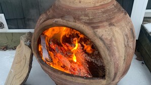 Un poêle à bois rustique, installé à l’extérieur sur une base en briques, avec un feu qui crépite à l’intérieur.